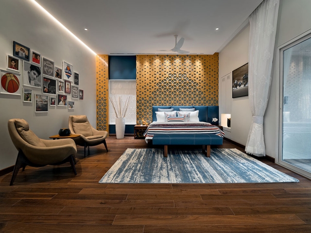 A bespoke bedroom with a geometric pattern on the walls, blue bedding and a sitting area accompanied by personal photo frames.