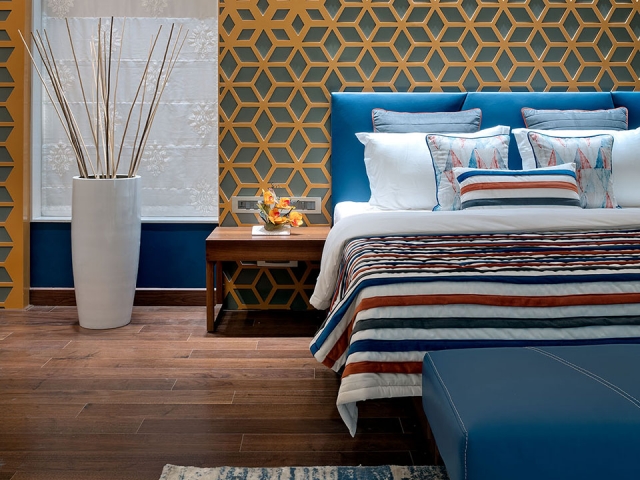 A bedroom with geometric patterns on the wall and wooden flooring along with blue bedding and furniture.