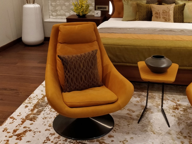 A close-up of a vibrant orange chair surrounded by other orange furniture and accessories in a room with dark wooden flooring.