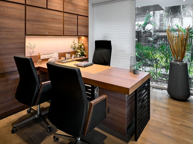 An elegant office space with wooden flooring and furnishings with a clear glass window overlooking a small patio filled with greenery.