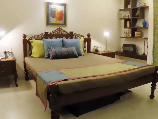 A large bed with a yellow and blue colour scheme for the bedding and wooden shelves on the wall.